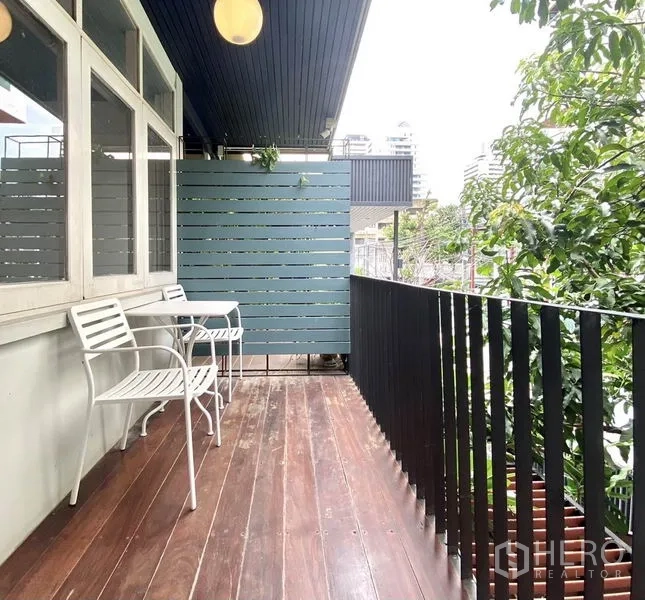 联排别墅 出租在Khlong Toei, Bangkok - 二层阳台木地板与黑色栏杆，设户外椅，绿意环绕。