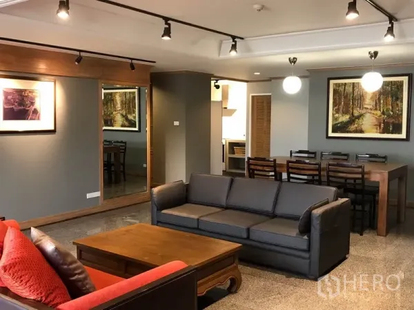 Condominium for sale in Watthana, Bangkok - Open-plan living and dining room with grey sofa, wood coffee table, track lights and large mirror in a Watthana condo.