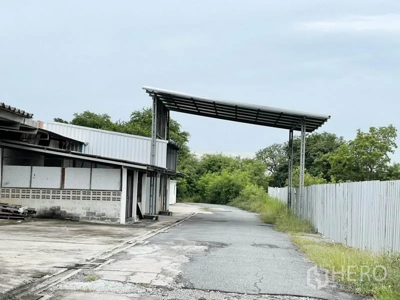 Factory for rent in Bang Pakong, Chachoengsao - Site driveway with a covered loading canopy and perimeter fence next to trees.