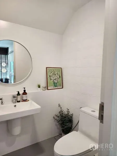 Detached House for rent or sale in Bang Phli, Samut Prakan - Bright powder room with white sink, round mirror and toilet in a modern Bang Phli house.