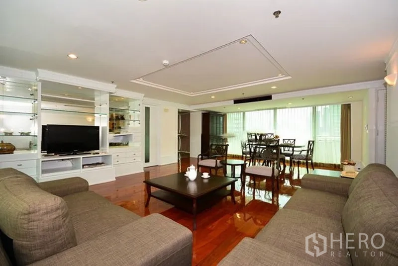Apartment for rent in Khlong Toei, Bangkok - Spacious lounge with built-in TV cabinet, sofa set and adjoining dining area on glossy wood floors.