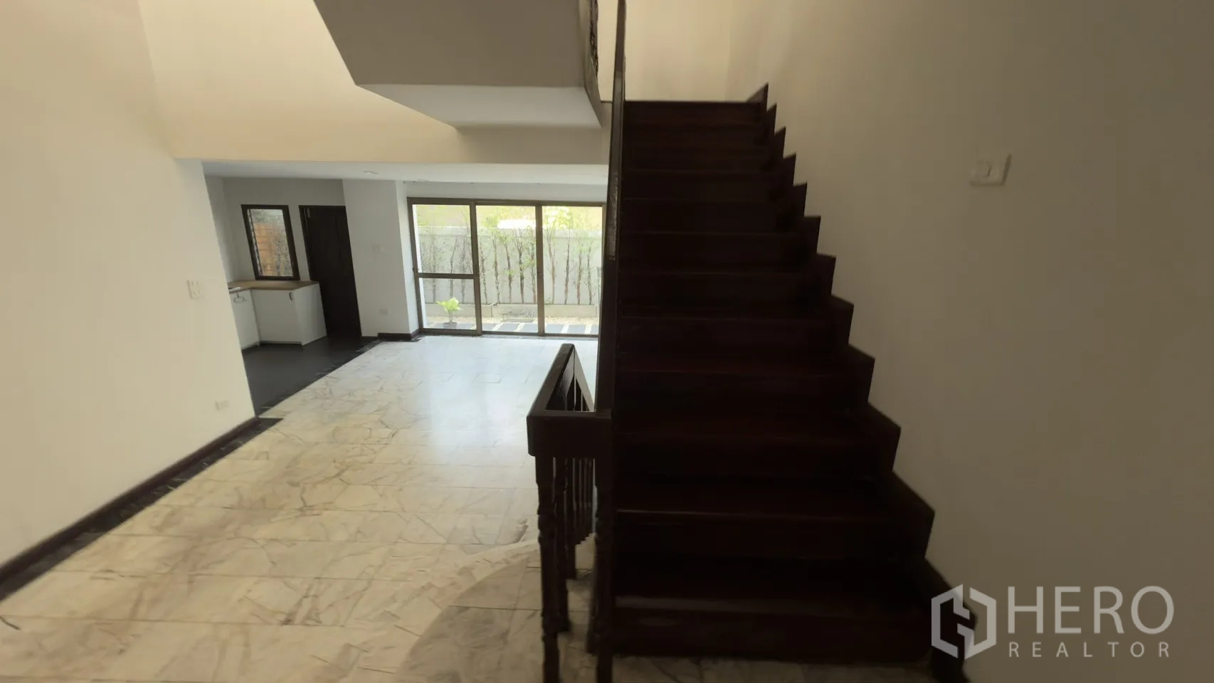 联排别墅 for rent in Watthana, Bangkok - 一层客厅铺大理石地面，木楼梯，落地玻璃门面向小花园。