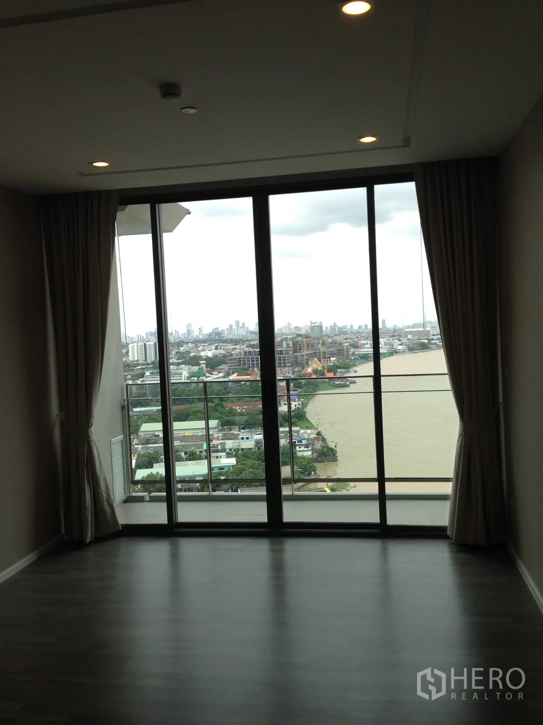 Condominium for rent in Bang Sue, Bangkok - Living area with floor-to-ceiling windows and balcony facing river and skyline.