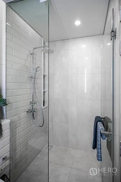 Condominium for sale in Khlong Toei, Bangkok - Modern shower with glass enclosure, rainfall showerhead, and white marble-effect and subway tiles.