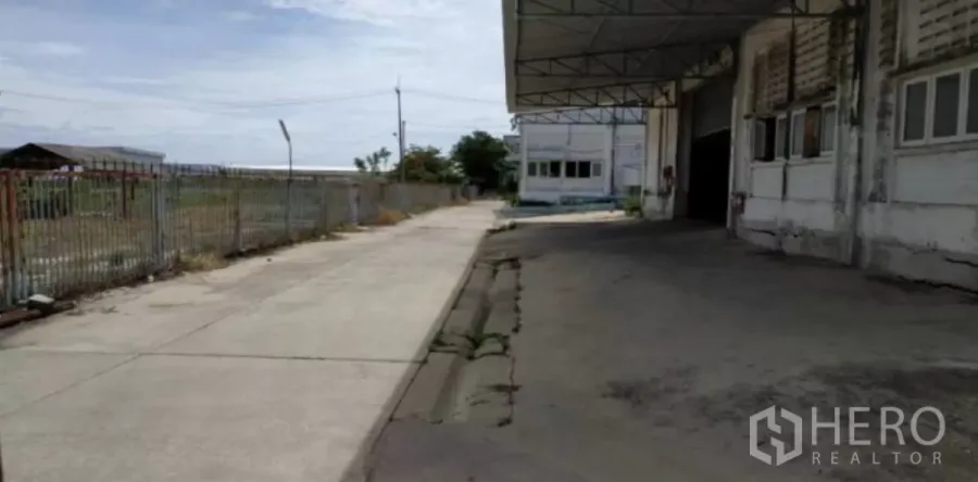 工厂 出租在Bang Pakong, Chachoengsao - 工厂建筑旁的有顶装卸区与混凝土车道，外侧为围栏。