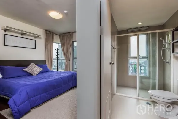 Condominium for rent in Bang Na, Bangkok - Master bedroom beside a bathroom with glass shower enclosure and window views.