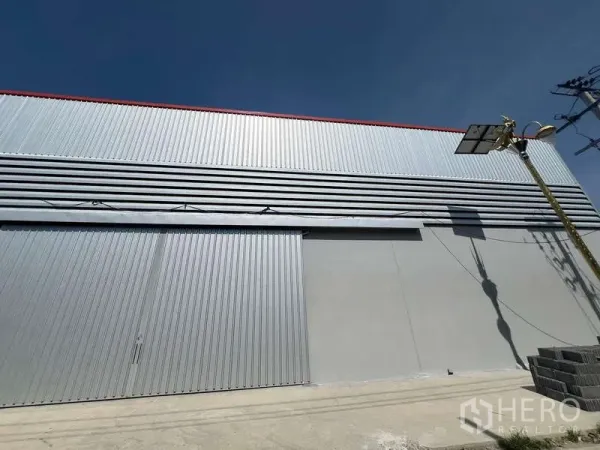 货栈 出租在Prawet, Bangkok - 仓库外立面的大型金属推拉门与通风百叶，晴空之下。