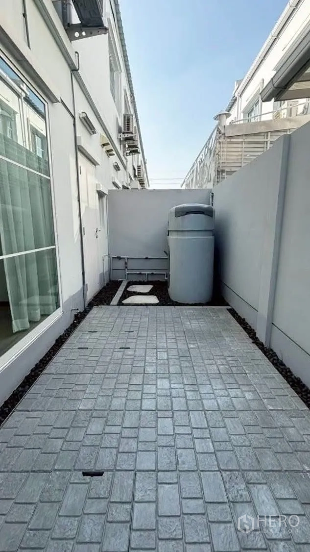 联排别墅 for rent in Prawet, Bangkok - 后院铺装生活区，设有水箱与侧面服务通道。