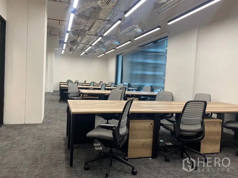สำนักงาน ให้เช่าในPathum Wan, Bangkok - พื้นที่ทำงานแบบเปิด โต๊ะไม้ยาว เก้าอี้เออร์โกโนมิก พื้นพรม โคมไฟเส้น LED และหน้าต่างบานใหญ่