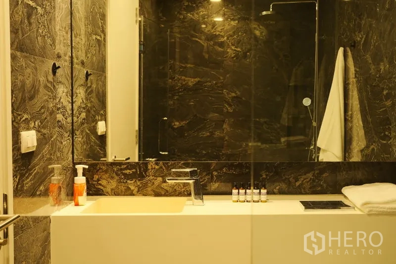 Condominium for rent in Bang Rak, Bangkok - Modern bathroom with marble-look walls, wide vanity and glass shower enclosure.