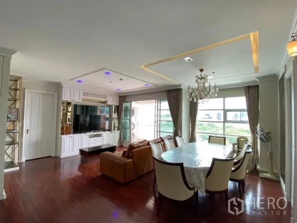 Condominium for rent in Ratchathewi, Bangkok - Bright lounge with built-in TV wall, large windows, dining table, and access to the balcony.