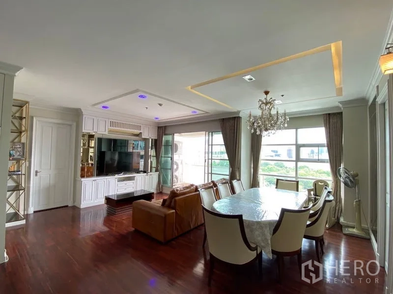Condominium for rent in Ratchathewi, Bangkok - Bright lounge with built-in TV wall, large windows, dining table, and access to the balcony.