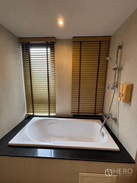公寓 出租在Watthana, Bangkok - 浴室配嵌入式浴缸、手持花洒和两扇带百叶窗的窗户。