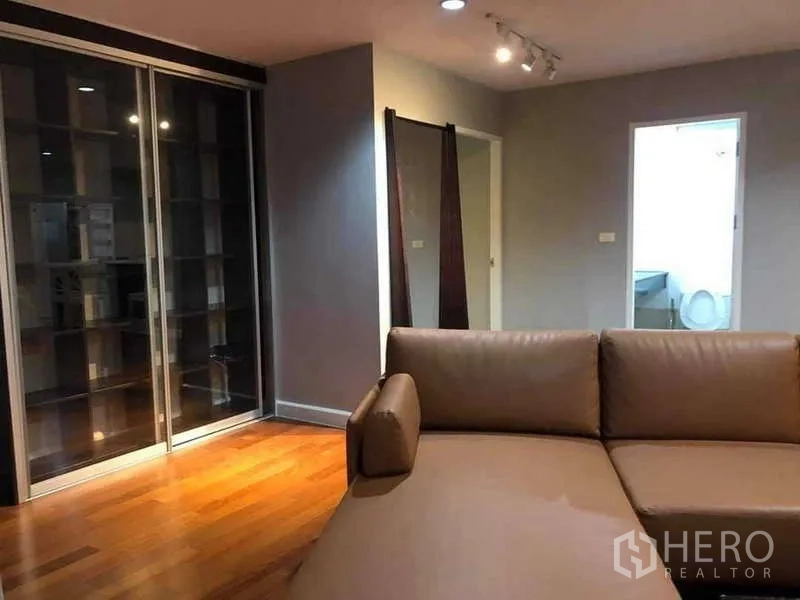 Condominium for sale in Yan Nawa, Bangkok - Living room corner with track lighting, shelving and doorway to a bathroom.