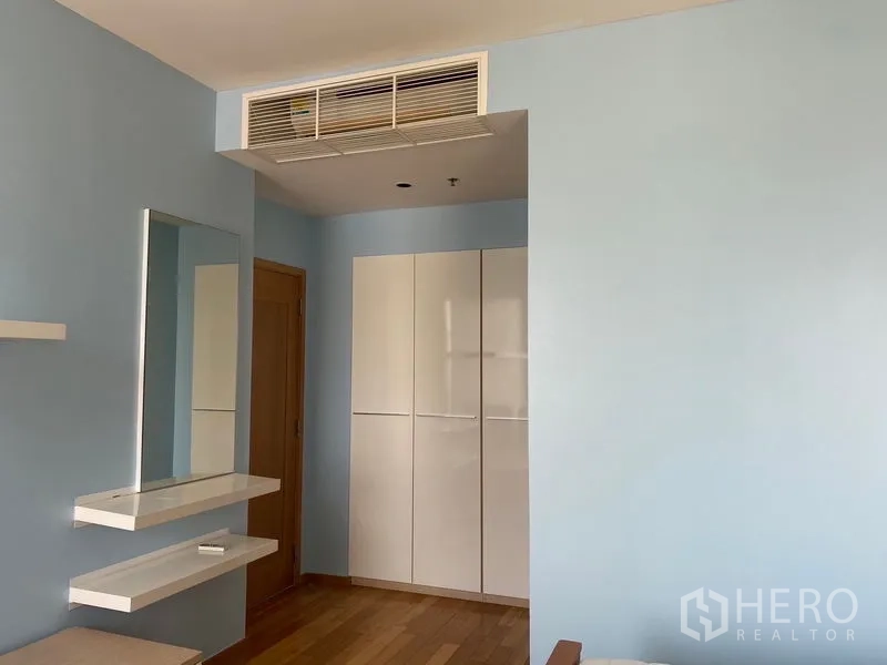 Condominium for rent - Bedroom corner with light blue walls, built-in wardrobe, wall shelves, and ceiling air-conditioning vent.