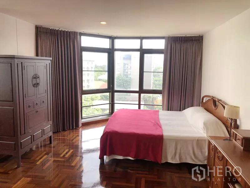 Condominium for rent or sale in Watthana, Bangkok - Spacious master bedroom with corner bay windows, double bed and wardrobe on parquet flooring.