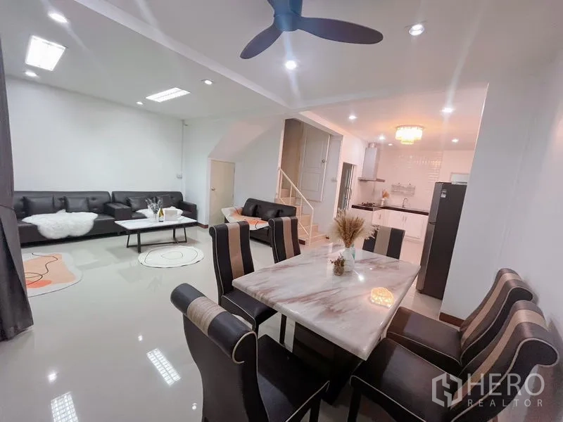 Townhouse for rent in Huai Khwang, Bangkok - Spacious living-dining room with marble table, ceiling fan and view to the kitchen.