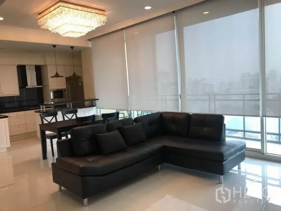Condominium for rent in Watthana, Bangkok - Living room with black sectional sofa, pendant lights, and full-height sliding glass doors.