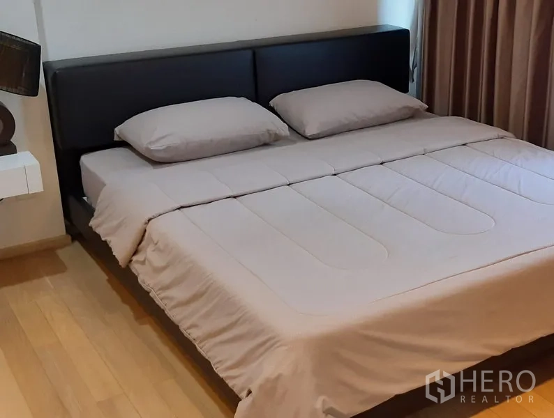 Condominium for rent in Khlong Toei, Bangkok - Cozy bedroom featuring a king-size bed, padded headboard, wood flooring and blackout curtains.