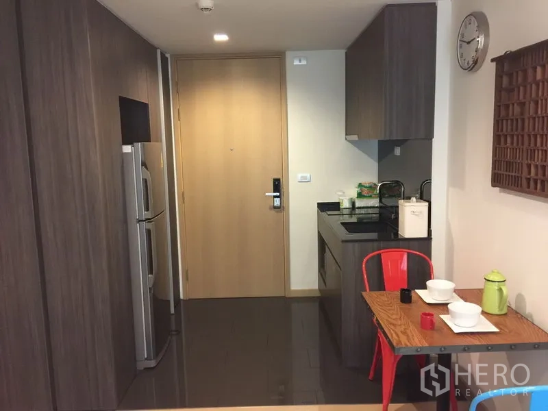 Condominium for rent in Watthana, Bangkok - Entry corridor with kitchenette, wooden front door, stainless refrigerator and two-seat dining table.
