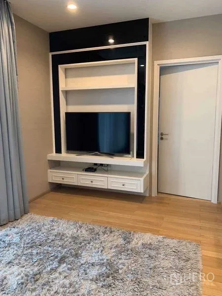 Condominium for sale in Watthana, Bangkok - Living room media wall with mounted TV unit, storage drawers and a plush area rug.