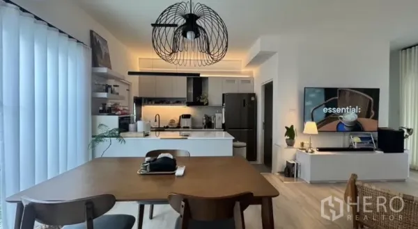 联排别墅 出租在Bang Phli, Samut Prakan - 明亮联排别墅的开放式餐厨空间，设中岛、现代橱柜、吊灯与电视墙。