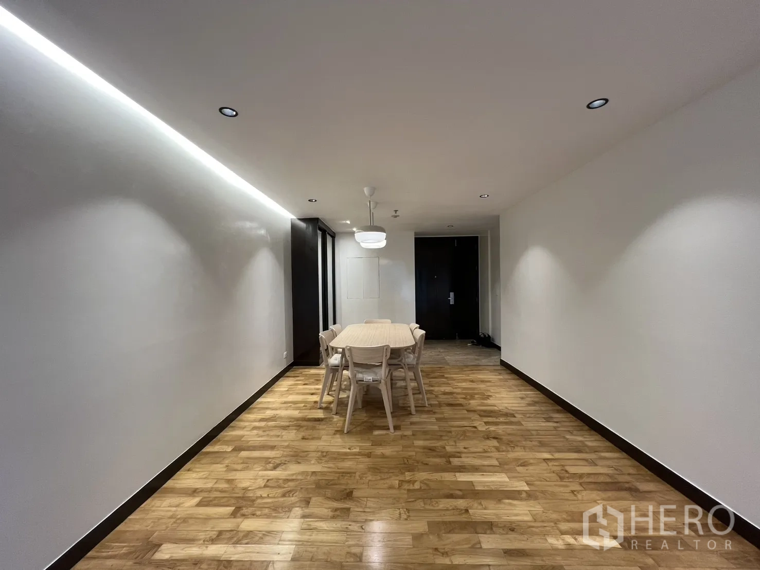 อพาร์ทเมนท์ for rent in Watthana, Bangkok - ภาพกว้างโซนรับประทานอาหารพร้อมไฟซ่อนบนฝ้า พื้นไม้ และประตูทางเข้าหลัก
