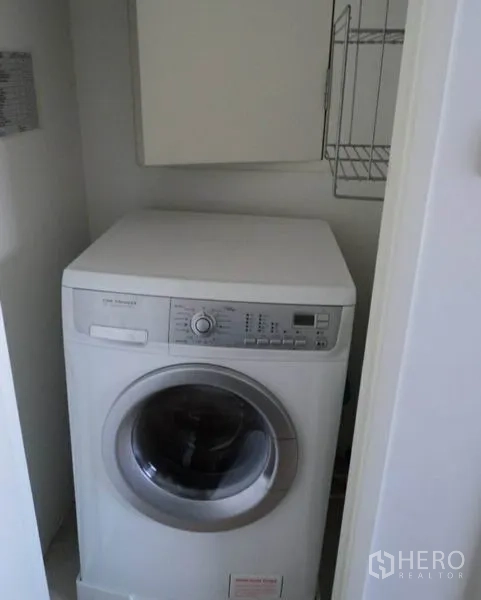 Condominium for rent in Khlong Toei, Bangkok - Laundry closet with front-load washing machine and storage shelves.