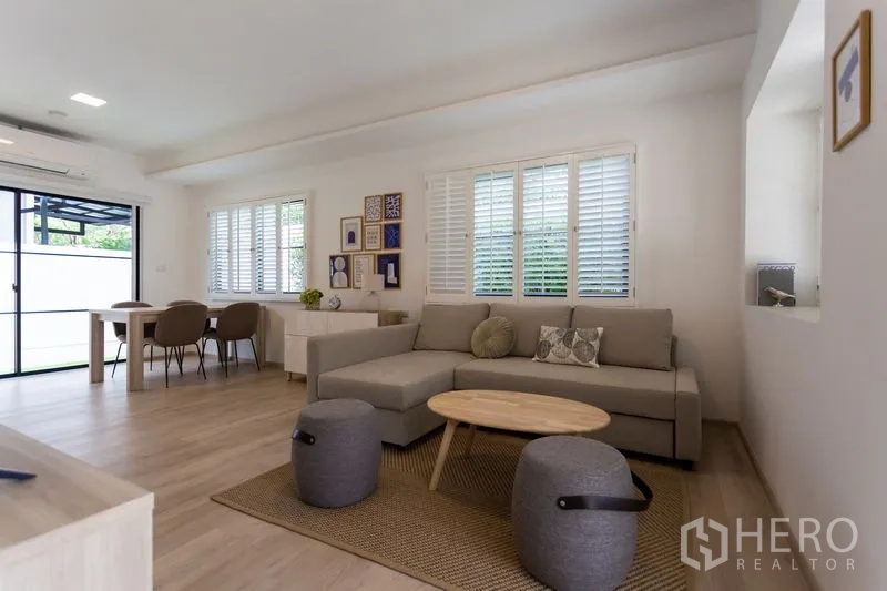 Townhouse for rent in Bang Phli, Samut Prakan - Open-plan lounge and dining area with corner sofa, gallery wall and sliding glass door.