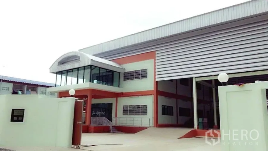 Factory for sale in Pathum Thani - Modern factory exterior with corner glass office, large roller shutter and ramp in Khlong Luang.