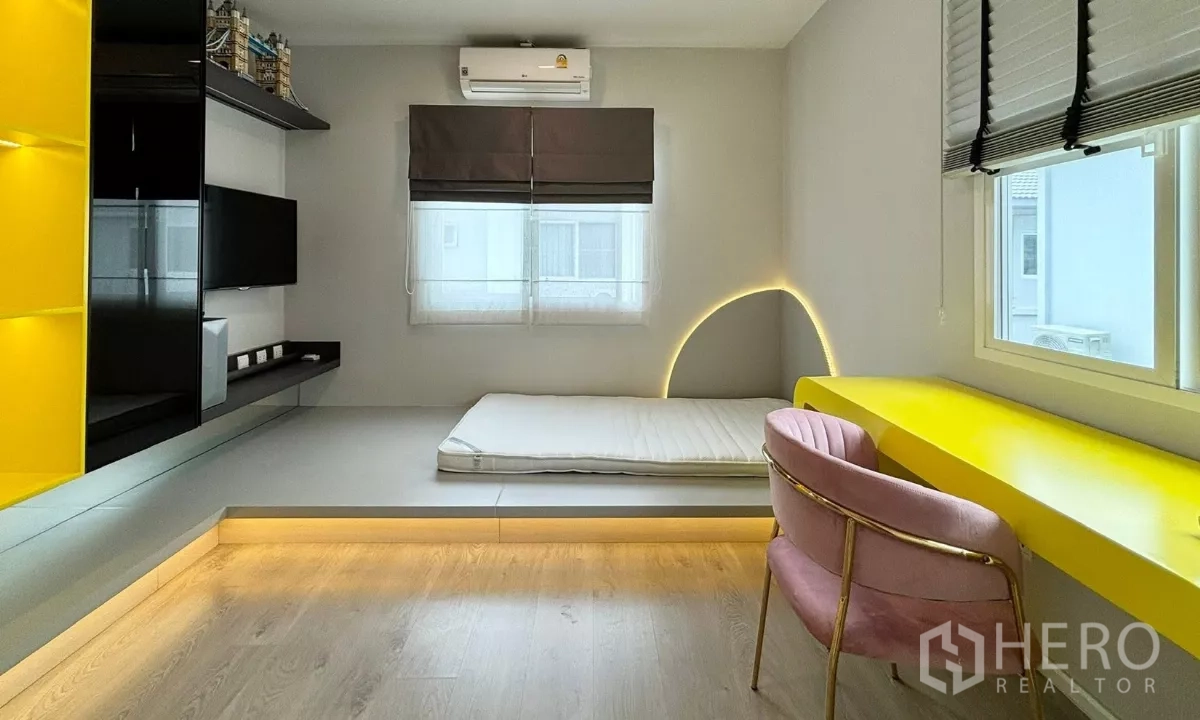 Detached House for rent or sale in Prawet, Bangkok - Kids or guest room with platform bed, bright yellow desk, pink chair and curved LED wall light.