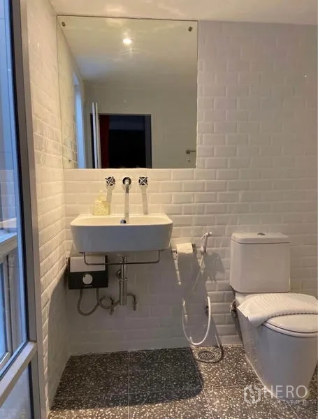 Townhouse for rent in Khlong Toei, Bangkok - Bright bathroom with white subway tiles, large mirror, wall‑mounted sink and toilet.