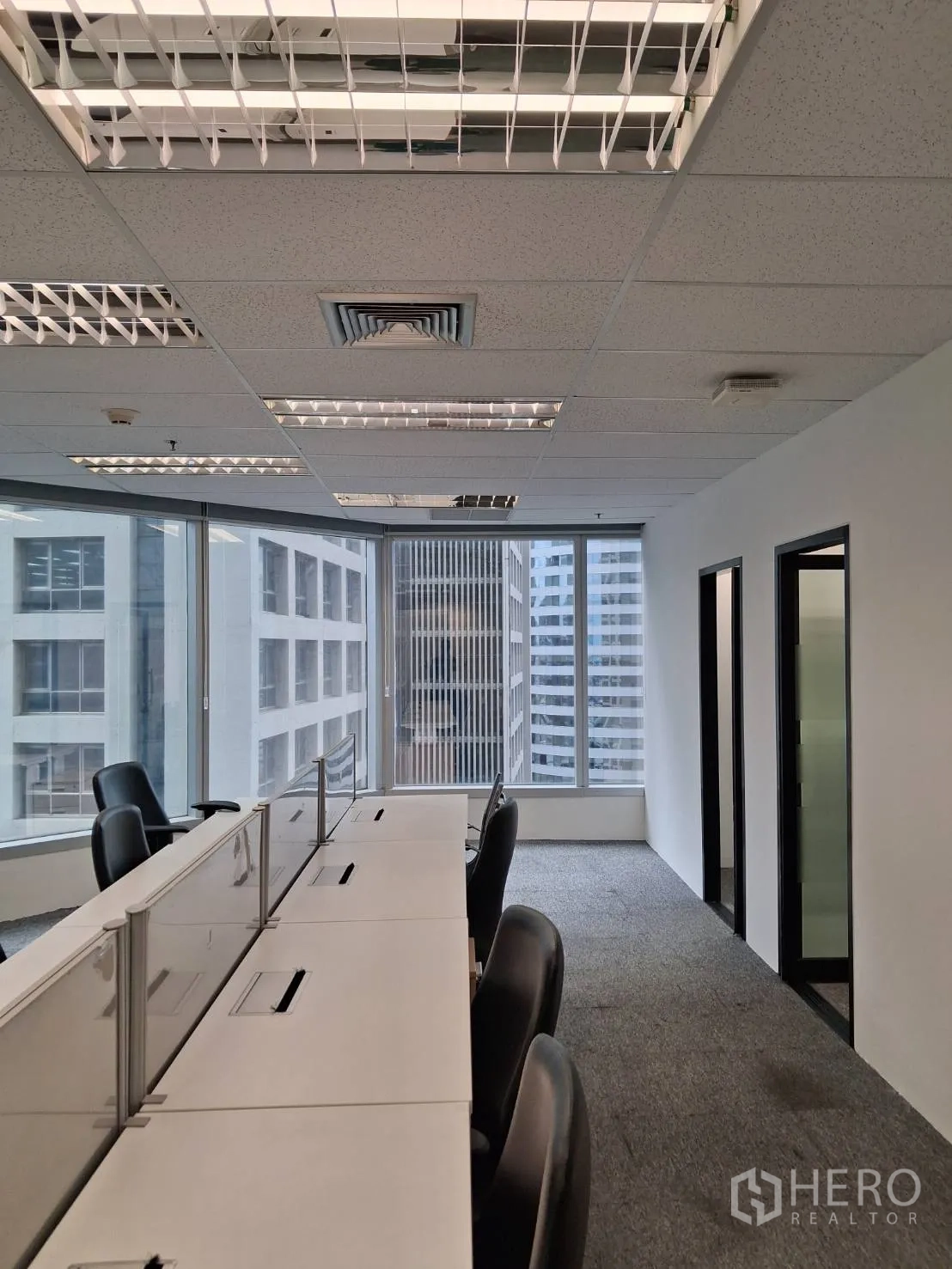 办公室 for rent in Sathon, Bangkok - 开放式办公区，长条工位、旋转椅、地毯地面与落地窗城市景观。