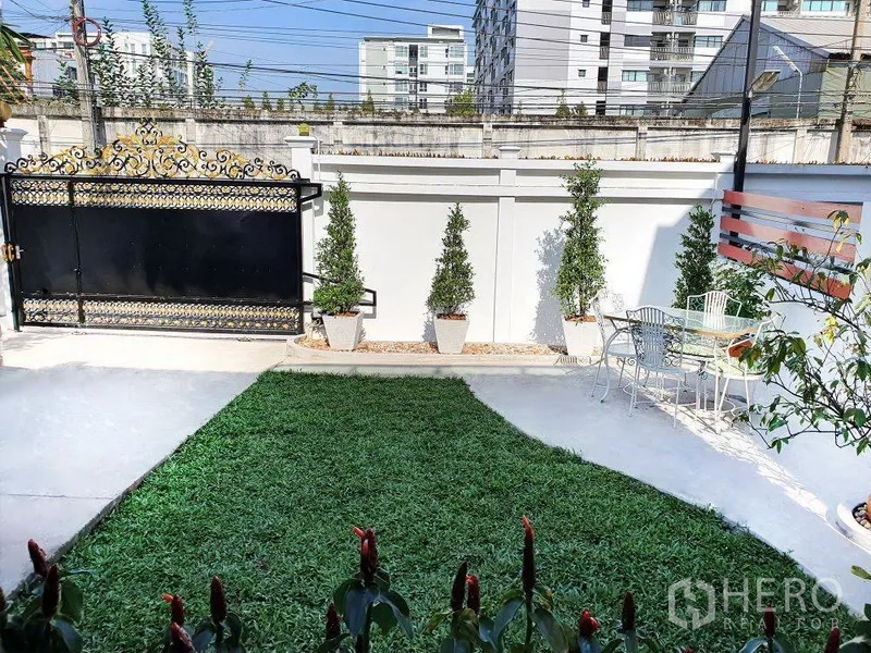 独立式住宅 出租在Phra Khanong, Bangkok - 前院草坪与盆栽，金色装饰大门，户外座椅。