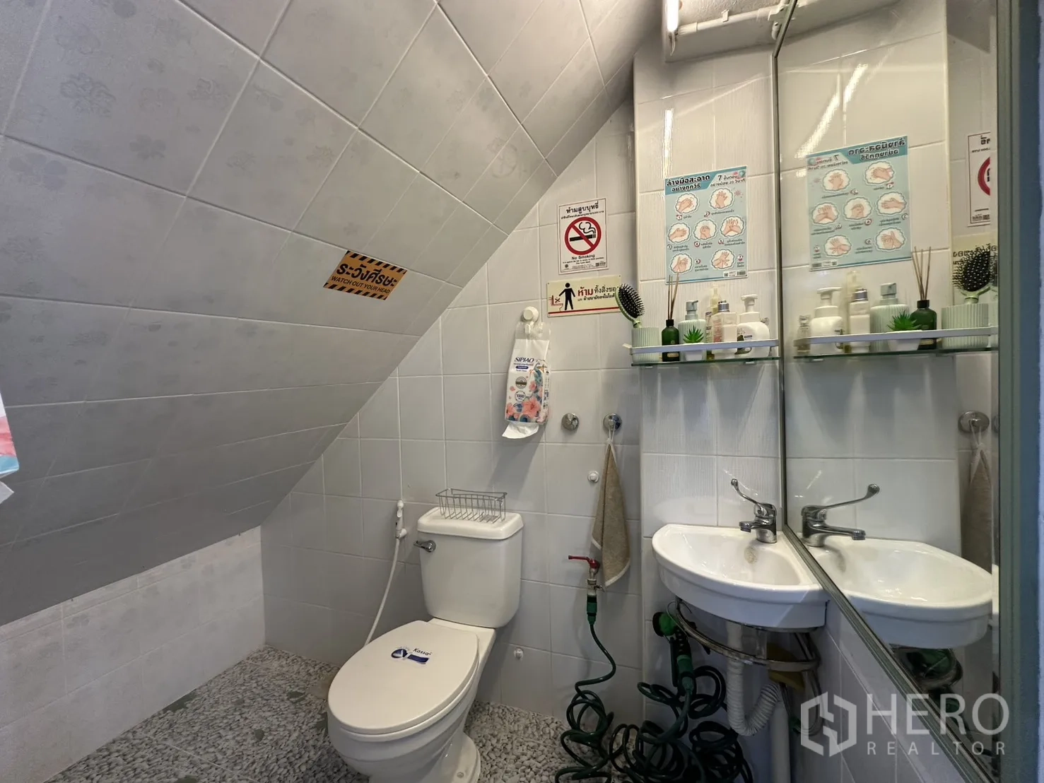 Shophouse for rent in Phra Khanong, Bangkok - Compact tiled bathroom with toilet, sink, and mirror.