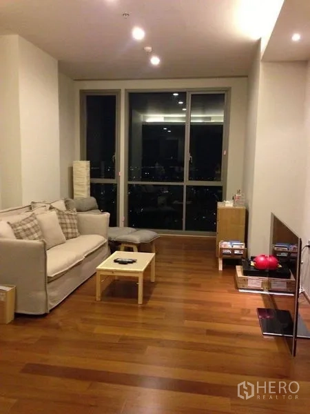 คอนโด ขายในWatthana, Bangkok - ห้องนั่งเล่นอบอุ่นมีโซฟา โต๊ะกลาง ชั้นวางทีวี และหน้าต่างบานใหญ่เห็นวิวสกายไลน์กลางคืน