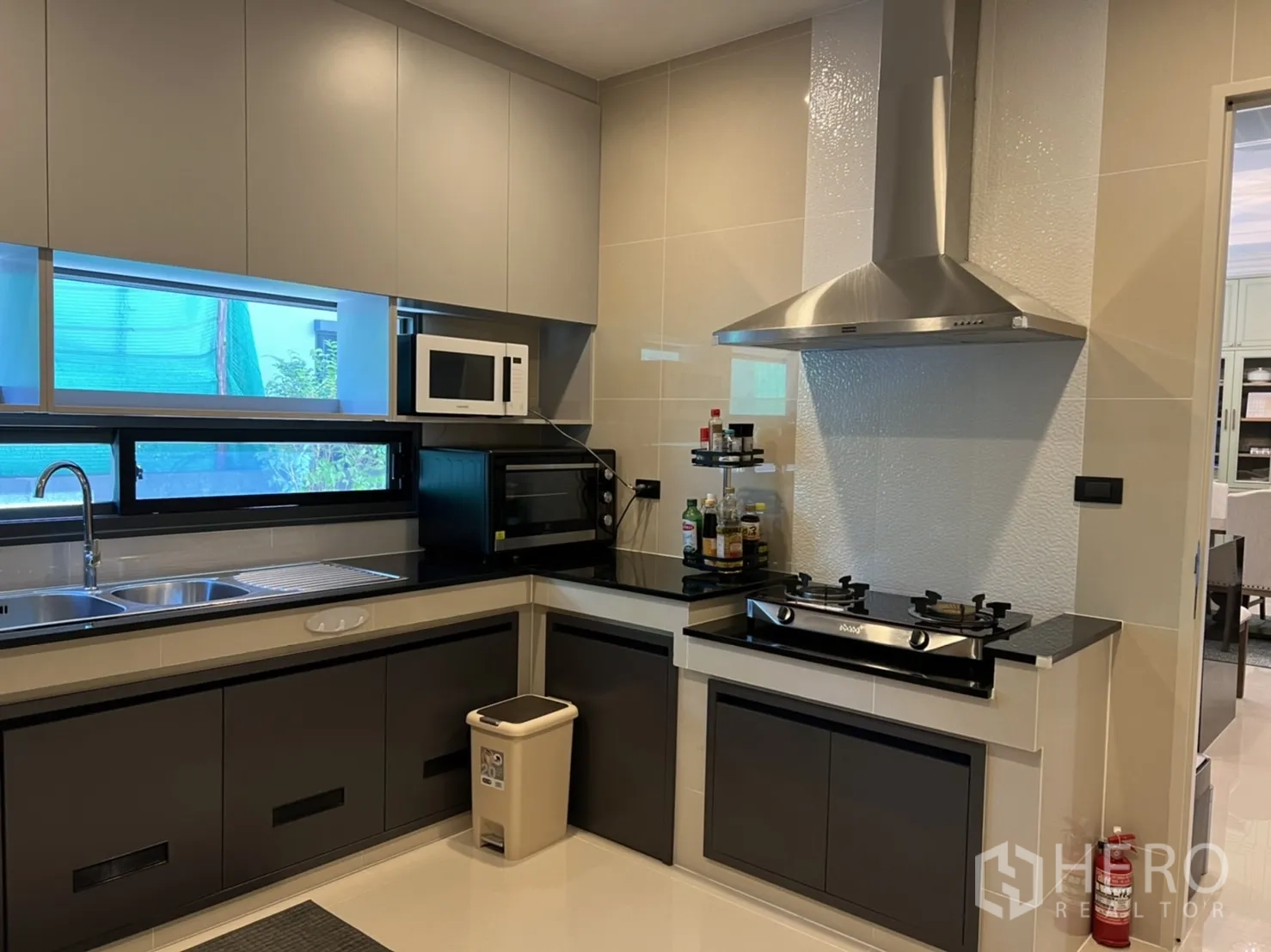 Detached House for rent or sale in Bang Kapi, Bangkok - Fully fitted Thai kitchen with L-shaped counters, double sink, gas cooktop with hood, microwave and oven by the window.