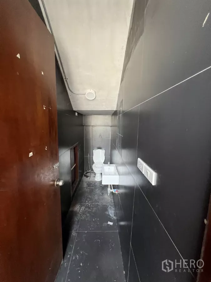 Retail Space for rent in Khlong Toei, Bangkok - Narrow restroom finished in black tiles with toilet and compact sink.