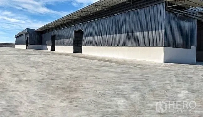 Warehouse for rent in Mueang Samut Sakhon, Samut Sakhon - Warehouse exterior with metal cladding, tall entry doors, and a wide concrete yard.