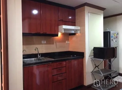 Condominium for rent or sale in Watthana, Bangkok - Kitchen wide view with fridge space and beige tiled walls.