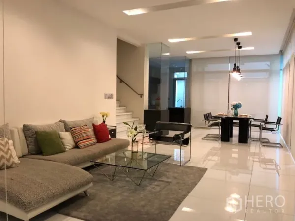 Townhouse for rent or sale in Chatuchak, Bangkok - Open-plan living and dining area with sectional sofa, glass coffee table and bright lighting.