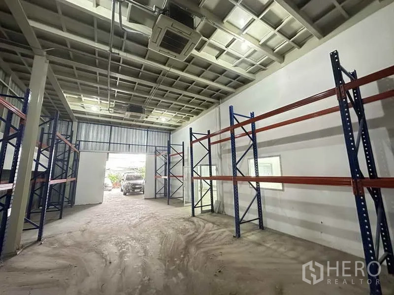 Home Office for rent in Bang Khen, Nonthaburi - Warehouse aisle with pallet racking and a high ceiling, vehicle visible at the wide doorway.