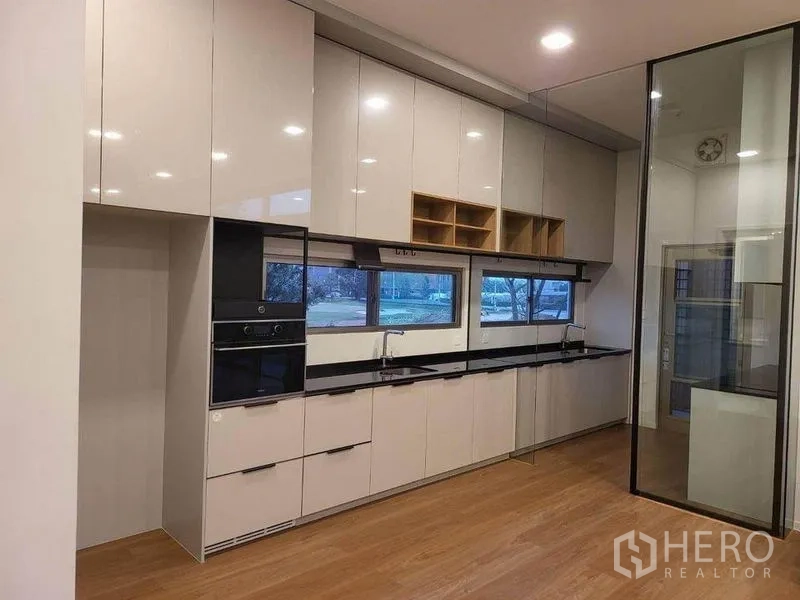 Detached House for rent in Saphan Sung, Bangkok - Sleek built‑in kitchen with glossy cabinets, black stone countertop, oven and glass partition.