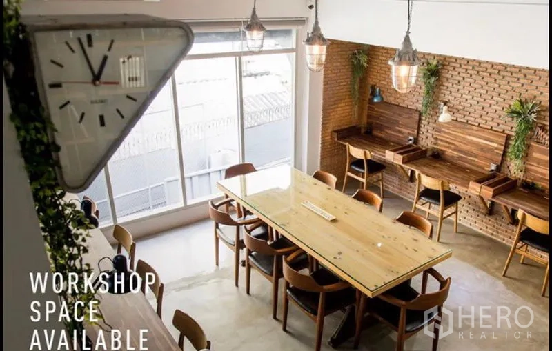 Home Office for rent in Khlong Toei, Bangkok - Bright coworking room with a long wooden table, brick feature wall, pendant lights and large windows.