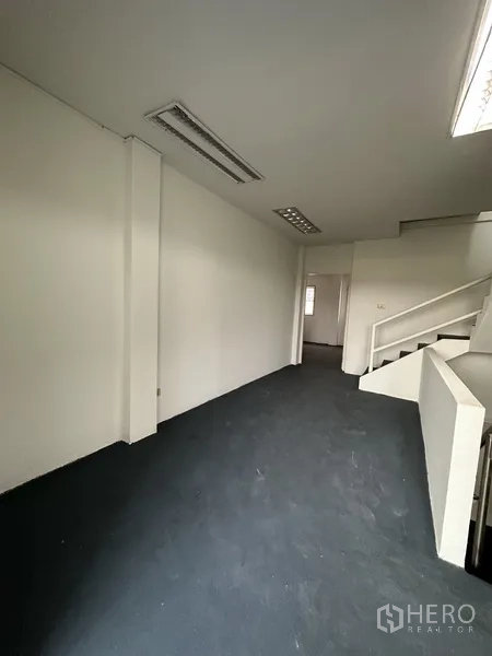 Shophouse for rent in Bang Na, Bangkok - Office-style corridor beside the stairwell with fluorescent lighting and dark flooring.