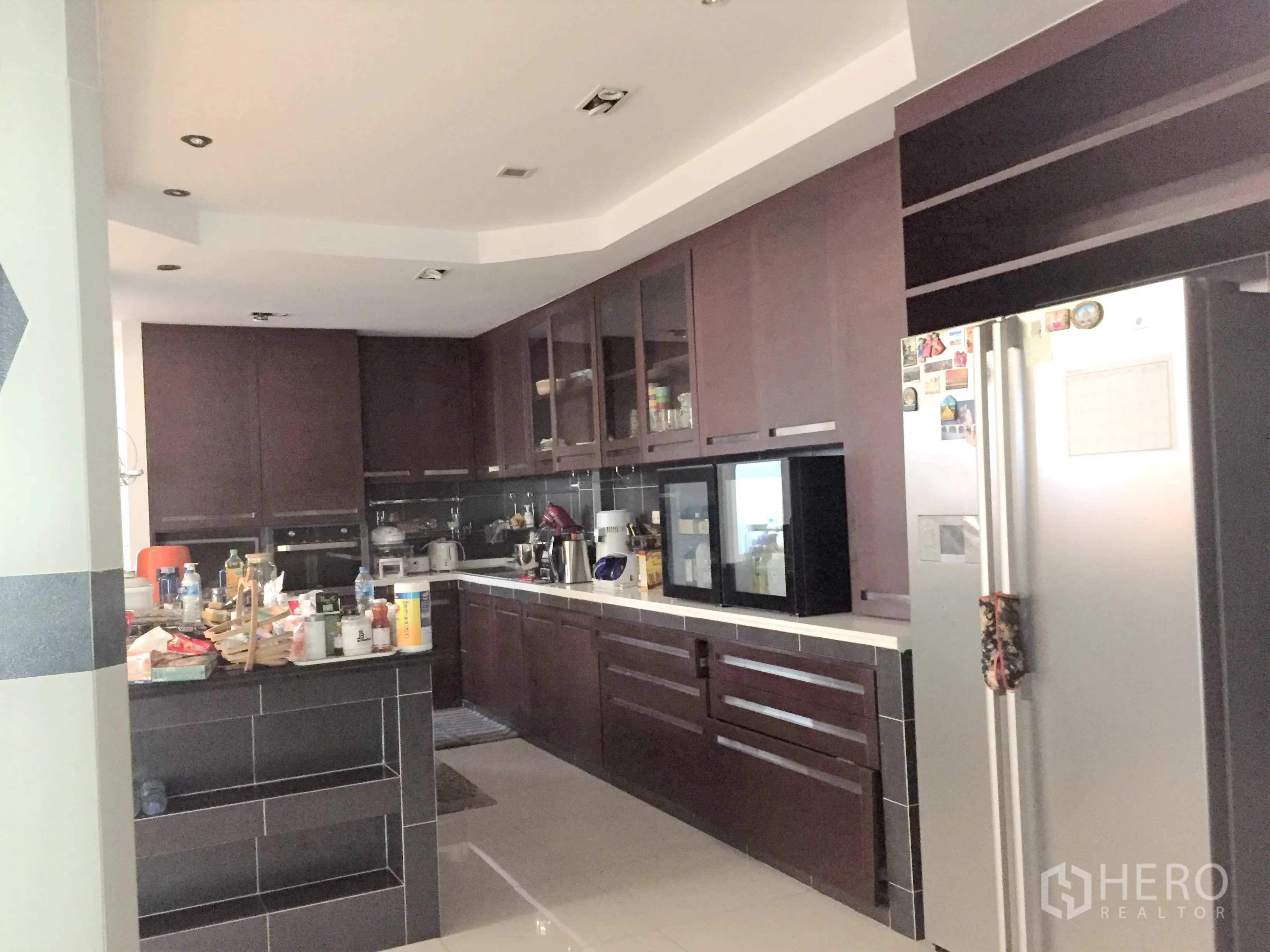 联排别墅 出租在Khlong Toei, Bangkok - 家庭厨房，深色木柜、岛台、嵌入式电器与不锈钢冰箱。