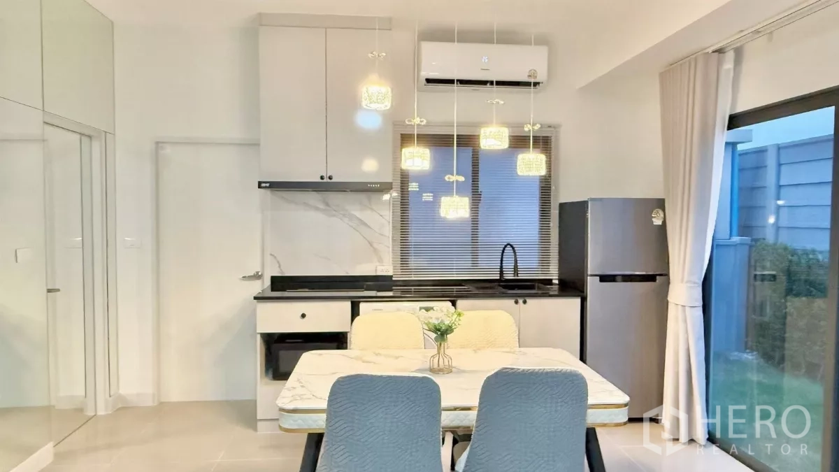 Townhouse for rent in Bang Phli, Samut Prakan - Compact white kitchen with black countertop, fridge and washer next to dining table.