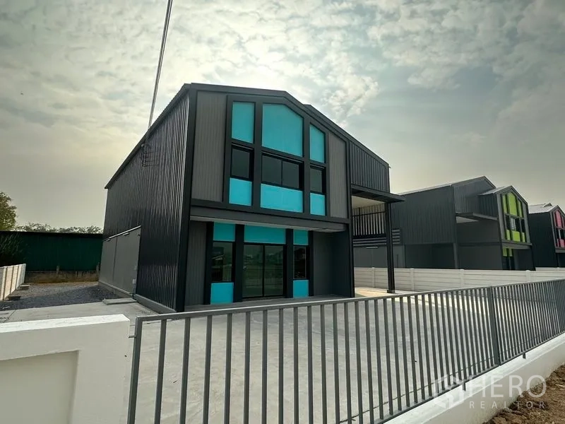 Factory for rent or sale in Bang Bua Thong, Nonthaburi - Row of new mini factories with fenced frontage and wide parking apron in an industrial enclave.