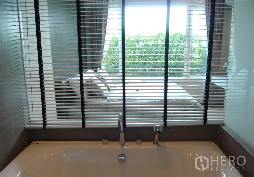 Condominium for rent in Khlong Toei, Bangkok - Modern bathtub with blinds looking through to the bedroom and garden view window.
