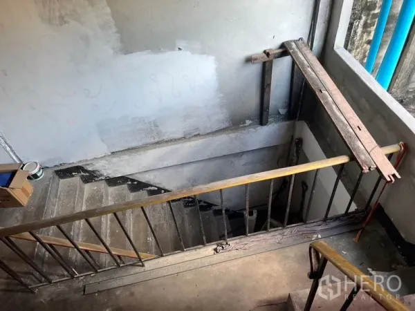 Shophouse for rent in Phra Khanong, Bangkok - Concrete stairwell under renovation with metal handrail and rough plaster walls.